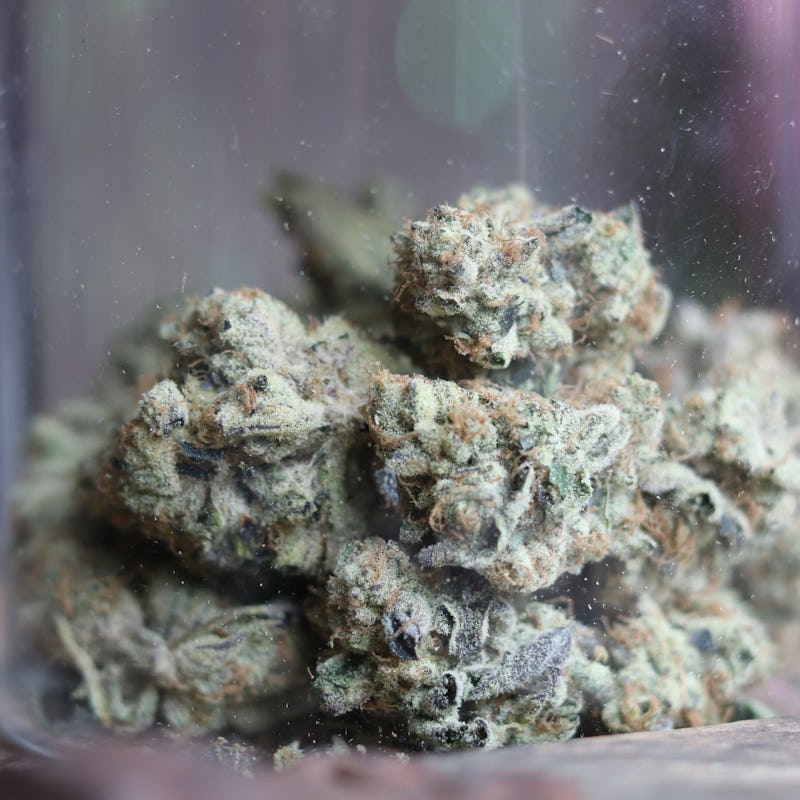 A up close photograph of an isolated glass jar of cannabis with a blurred background. Crystal tricho...