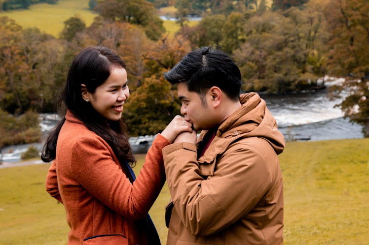 Happy attractive Asian couple fall in love, man hold woman hand kiss with diamond ring after make pr...
