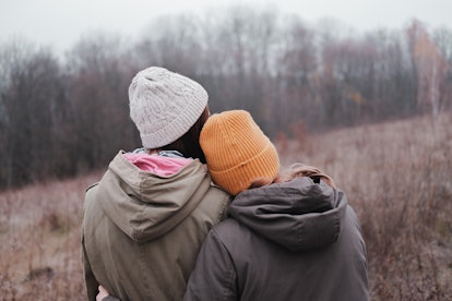 Two young girls in parka coats and knitted hats hug each other on autumn forest background. Concept ...