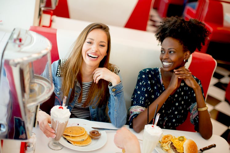 Multiracial female friends eating fast food at a table in the diner and have fun
