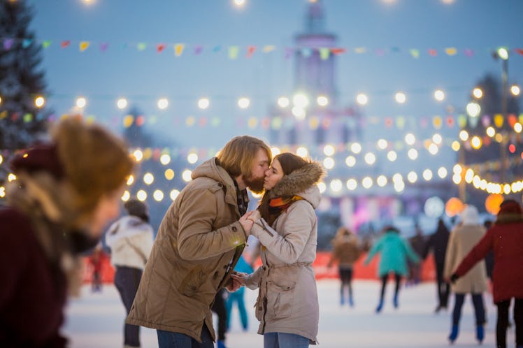 A young couple shares a kiss in the middle of an outdoor ice rink.