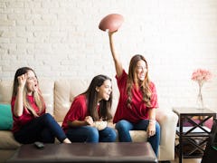 Three roomies wearing team jerseys and watching a football game on TV cheer on the couch.