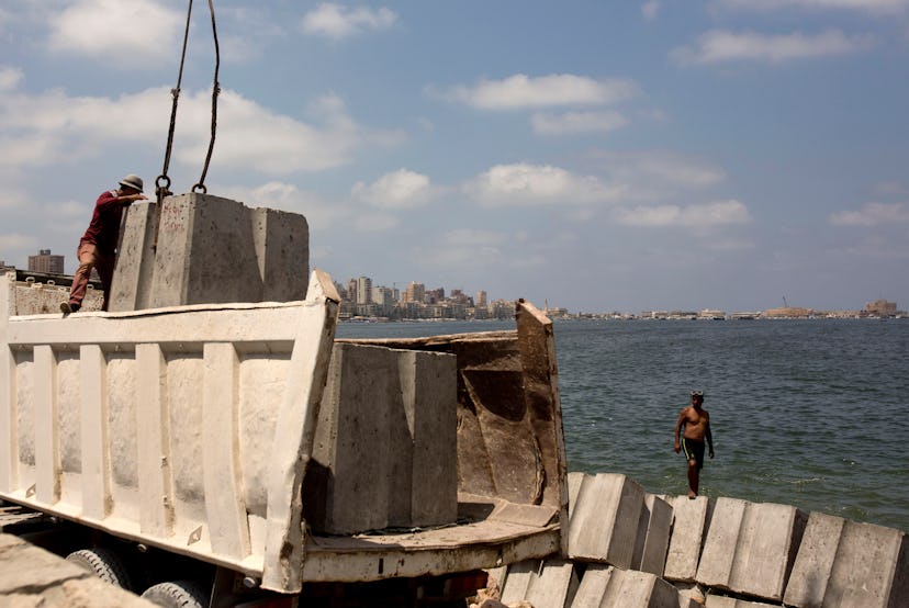 Workers prepare to place cement blocks to reinforce the sea wall against rising water levels on the ...