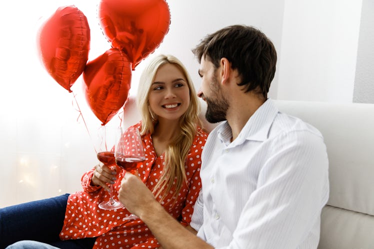 A woman and man clink their wine glasses while looking at each other on a couch on Valentine's Day.