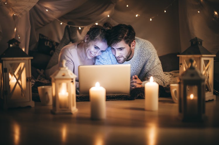 Man and woman lying on bed watching a movie on laptop at night in a decorated room. Couple using lap...