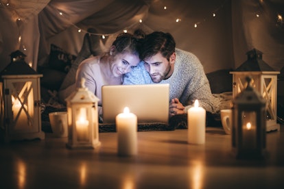Man and woman lying on bed watching a movie on laptop at night in a decorated room. Couple using lap...
