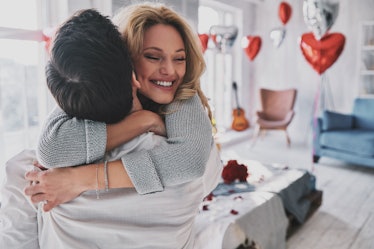 A happy blonde woman hugs her boyfriend who is lifting her up in the bedroom on Valentine's Day.