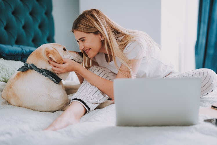 A happy woman in PJs cuddles with her dog on her bed.