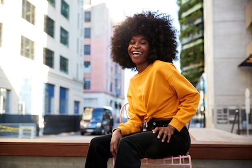 Young black woman with afro hair sitting on a chair in the street laughing to camera
