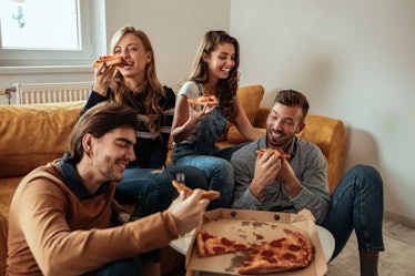 Two couples laugh and enjoy pizza in a bright living room.