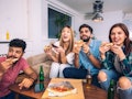 A group of friends enjoy pizza on the couch while watching the football game on TV. 