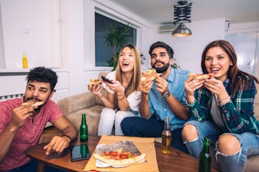 A group of friends enjoy pizza on the couch while watching the football game on TV. 