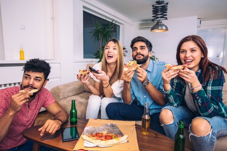 A group of friends enjoy pizza on the couch while watching the football game on TV.