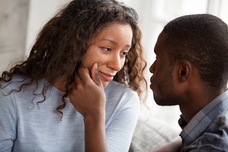 Loving African American man cheering beloved woman touching her face relaxing together at home, cari...