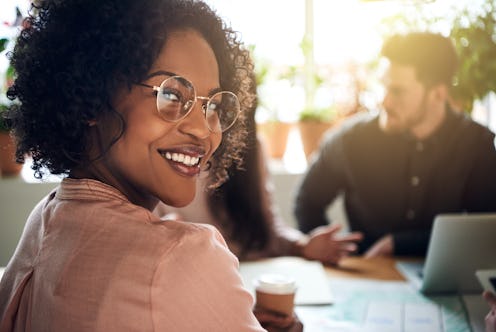 Smiling African businesswoman looking over her shoulder while sitting at a boardroom table with coll...
