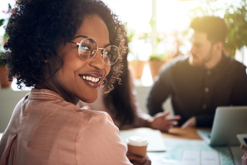 Smiling African businesswoman looking over her shoulder while sitting at a boardroom table with coll...