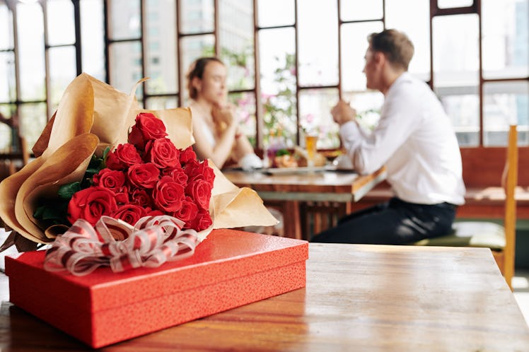 Horizontal shot of beautiful red roses and box of chocolate lying on cafe table, couple dating on ba...