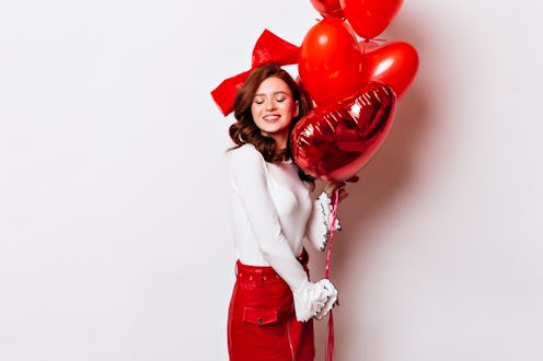 Happy ginger girl posing after date. Studio shot of european female model with red heart balloons.