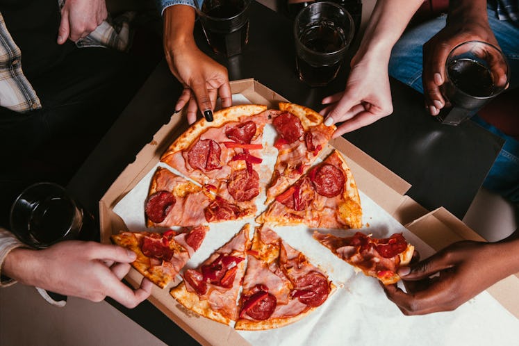 A group of friends' hands digs into a pepperoni pizza.