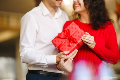 Man gives to his woman a gift box with red ribbon. A loving couple cuddles and celebrating Valentine...