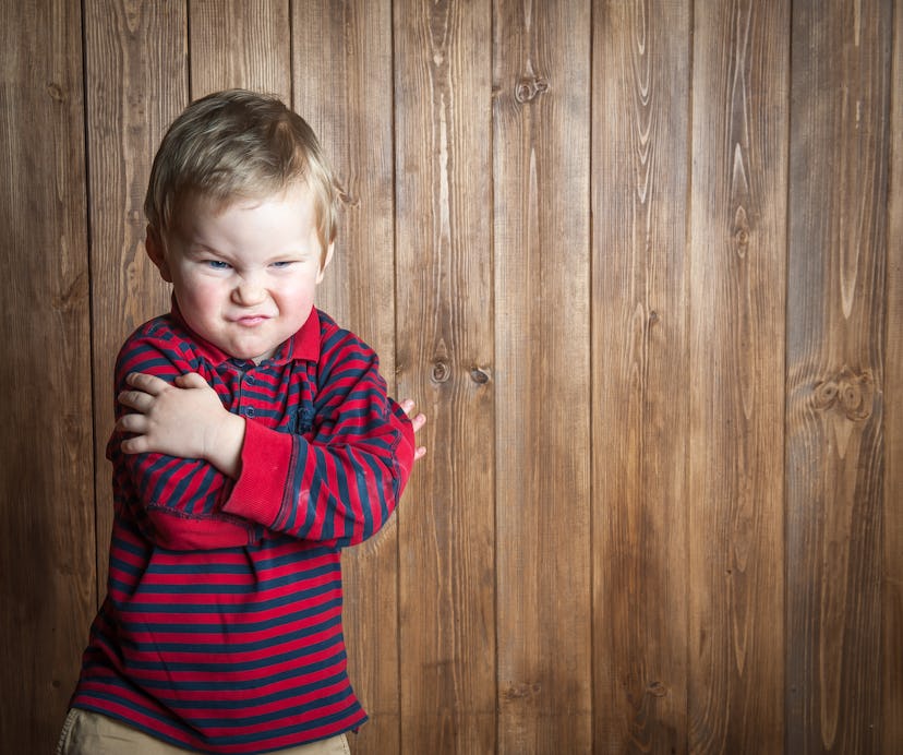 Very angry little boy. Cute toddler child is looking at camera. On wooden background. Space for text...