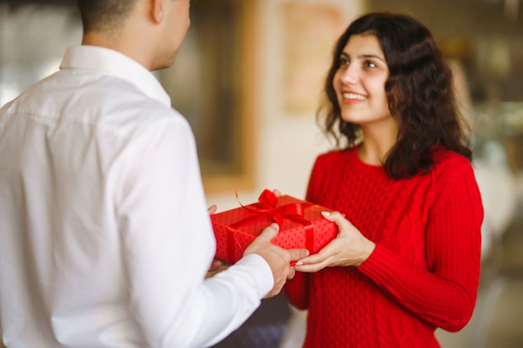 Man gives to his woman a gift box with red ribbon. A loving couple cuddles and celebrating Valentine...