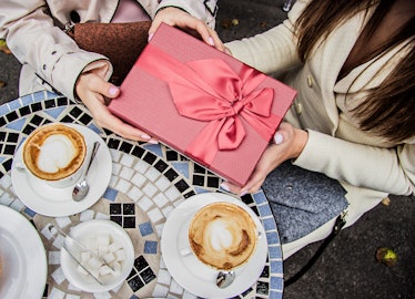 Top view of a woman giving her friend a pink present at a mosaic coffee table.