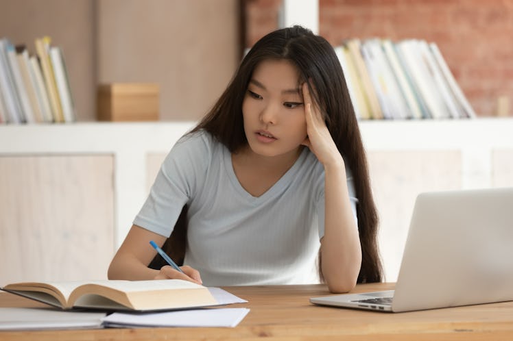 Tired young asian female student preparing for college test or writing abstract at library. Stressed...