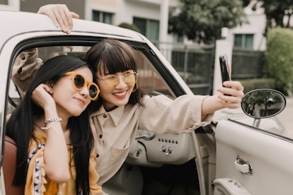 Two fashionable girls pose for a selfie on the seat of a car.