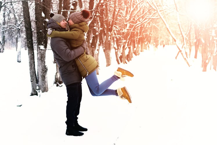 A happy couple embraces in the snow on a sunny day.