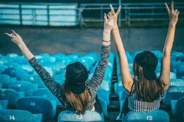 Two women wearing backwards baseball caps cheer on their team in the bleachers.