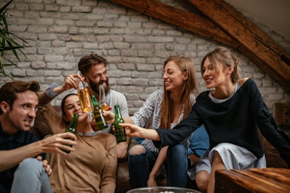 A group of friends clink their beer bottles while hanging out at home.