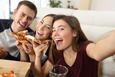 Three friends smile and pose for a selfie with their slices of pizza.