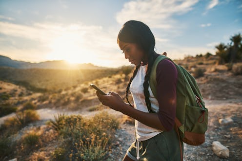 athletic african american woman with backpack looking at smart phone while hiking in red rock canyon...