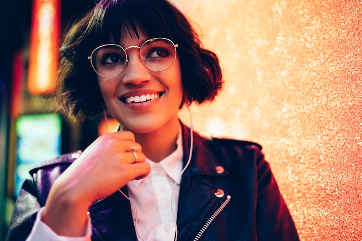 Dreamy pretty hipster girl in stylish lather jacket and fashionable eyewear listening electronic aud...