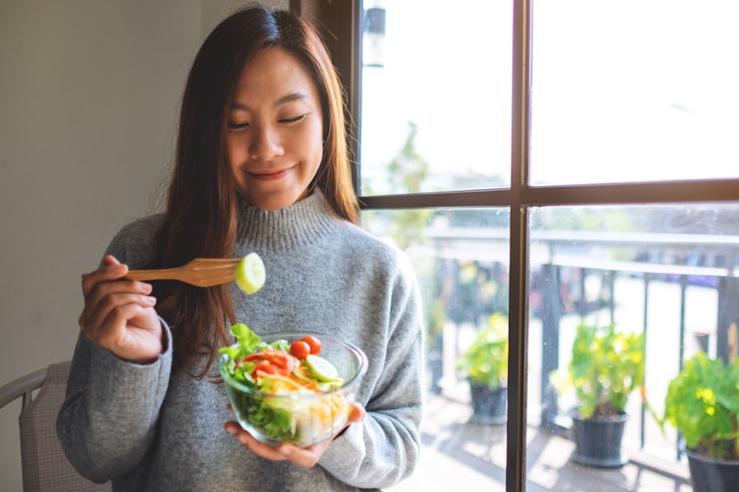Closeup image of a beautiful asian woman eating and holding a bowl of fresh mixed vegetables salad