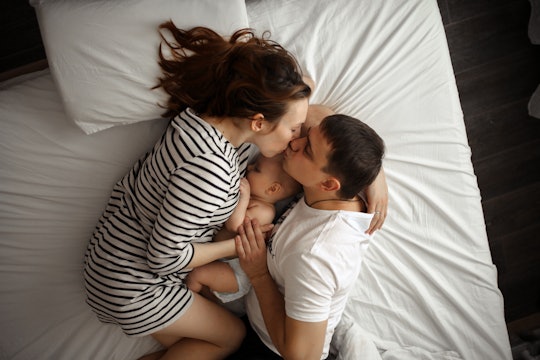 A mom breastfeeding her baby in bed while kissing her husband