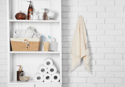 Bathroom set with towels, toothbrushes and basket on a shelf in light interior