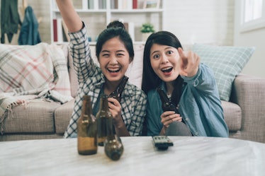 two excited asian women cheerful laughing celebrating victory win watching games on television tv po...