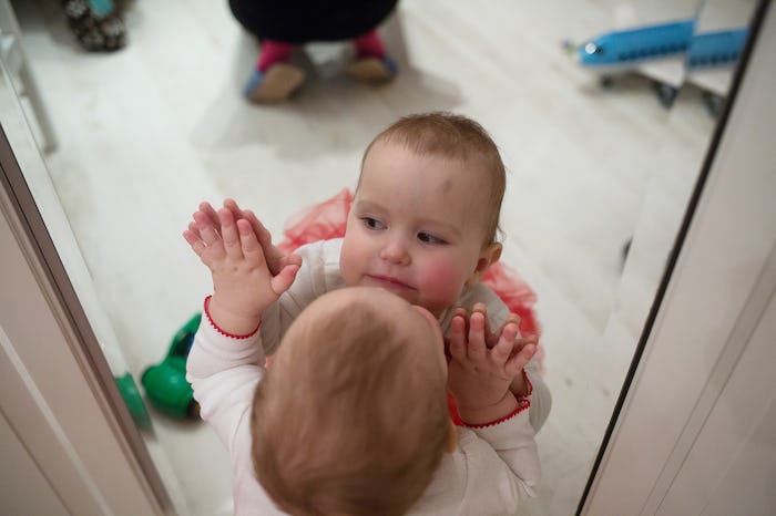 One-year-old girl looks at herself in the mirror