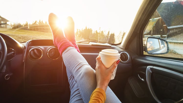 Young woman drinking coffee inside car in fall season - Girl relaxing and enjoying sunset traveling ...