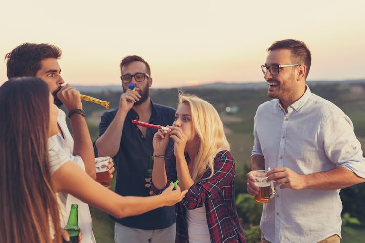 A group of friends have fun while blowing party whistles and drinking beer outside.