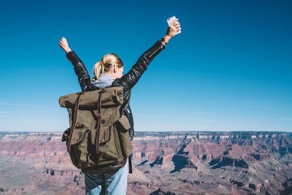 A girl stands with her phone and a backpack on the top of the Grand Canyon.