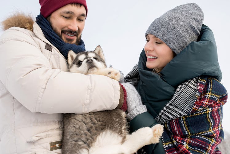 A couple who's all bundled up for the cold weather cuddles with their puppy outside.