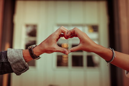 Holding hands together. Positive couple connecting fingers and creating heart shape while having hou...