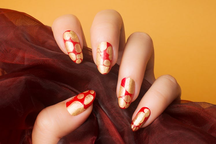Female hand with red gold nails on orange background, nail care and manicure concept.
