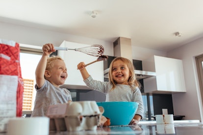 Cute little boy and girl fighting with whisk and spatula while mixing batter in a bowl. Siblings enj...