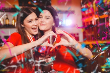 Confetti party. Two young lesbian girls make a heart with their hands at a club party.