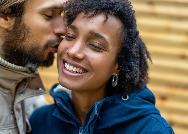 A woman closes her eyes and smiles while her boyfriend kisses her cheek.