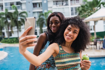 Two best friends in swimsuits smile and take a selfie by the pool. 